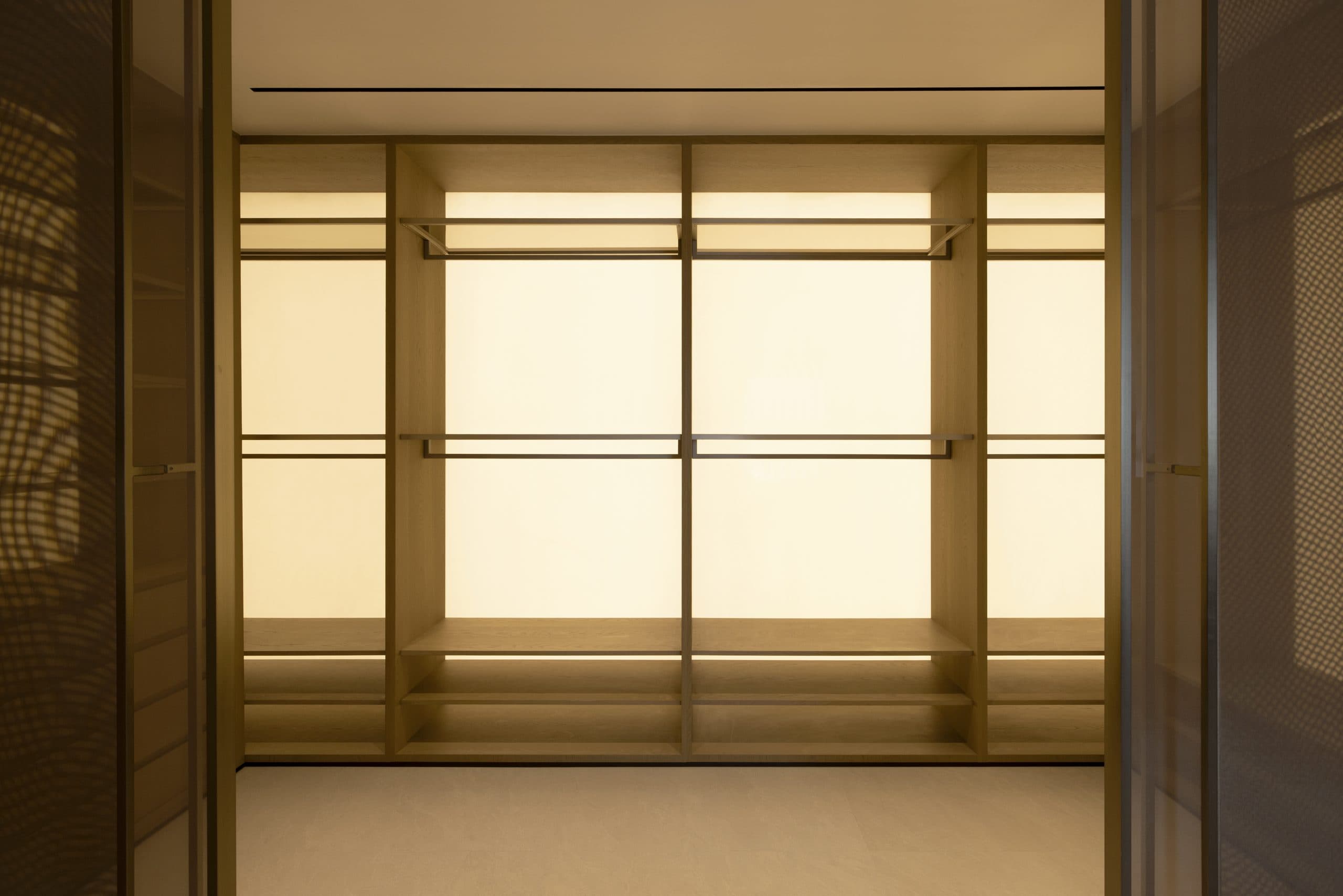 Walk-in wardrobe in oak with backlit panels, hanging rails and bronze glass doors
