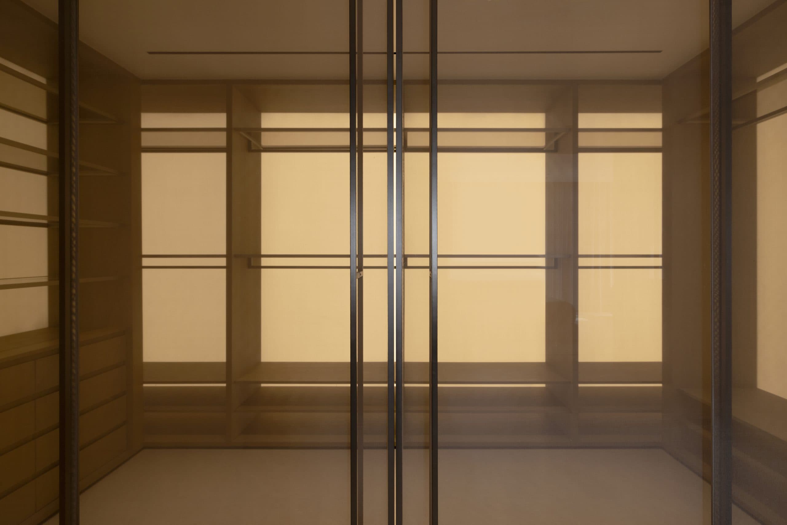 Walk-in wardrobe in oak with backlit panels behind bronze glass doors