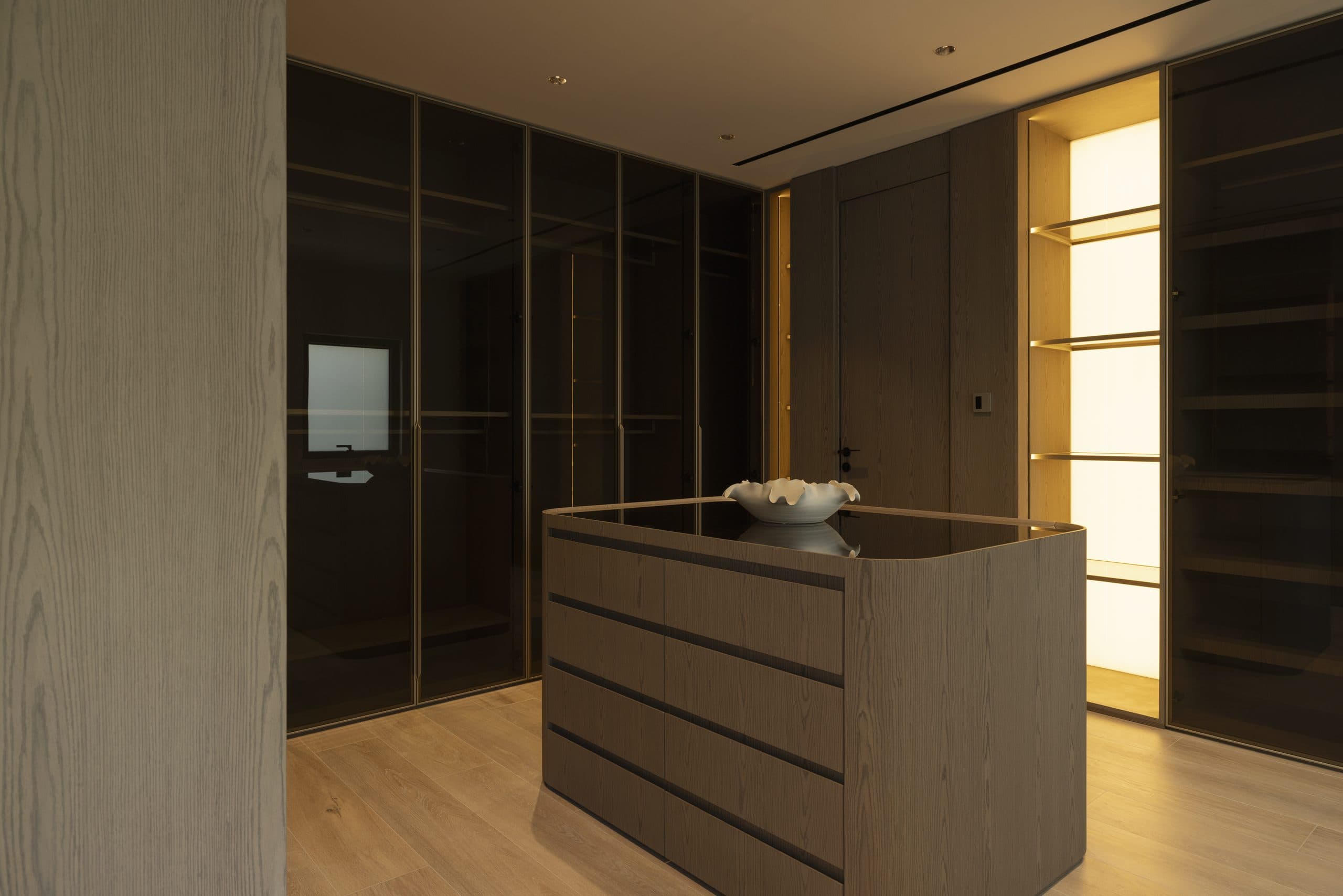 Dressing room with smoked glass wardrobe fronts, backlit shelving and an oak island