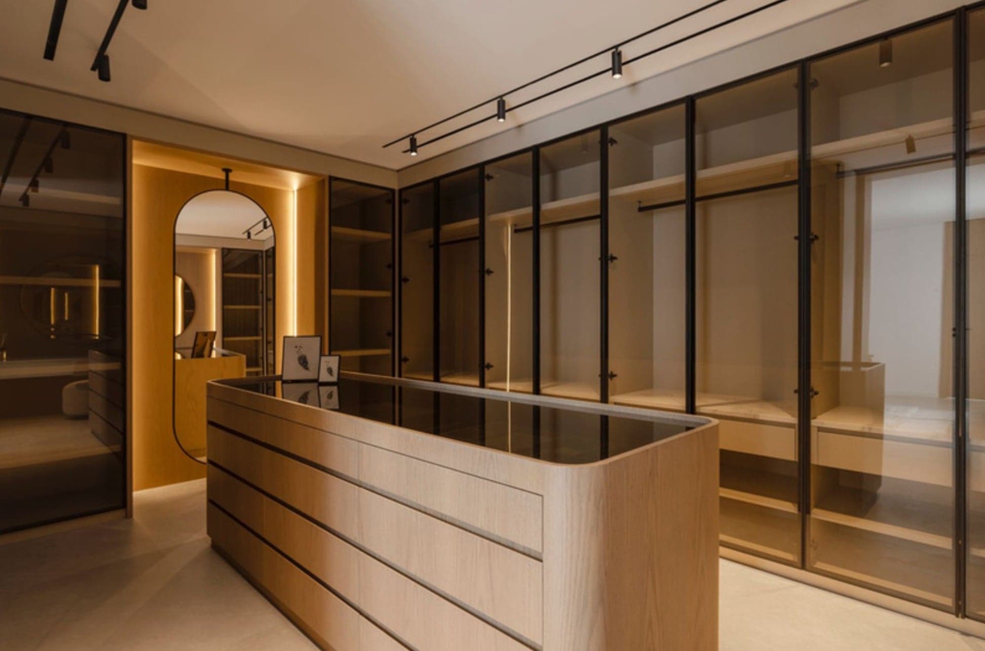 Walk-in wardrobe with framed glass-front cabinetry, a central island dresser and warm integrated lighting
